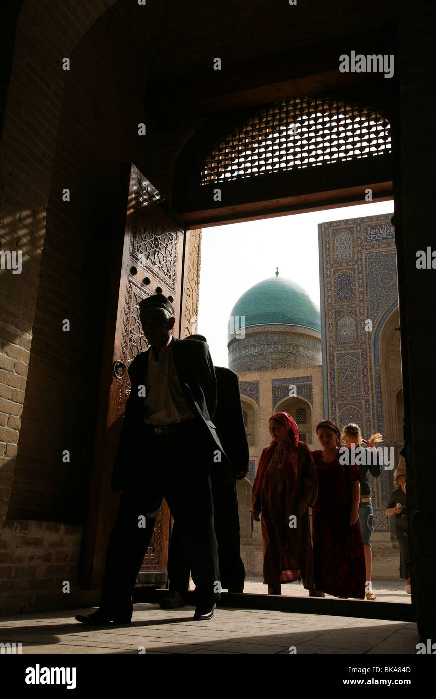 Uzbek persone che entrano per la moschea Kalyan a Bukhara, Uzbekistan. Mir-ho Arab madrasa è in background. Foto Stock