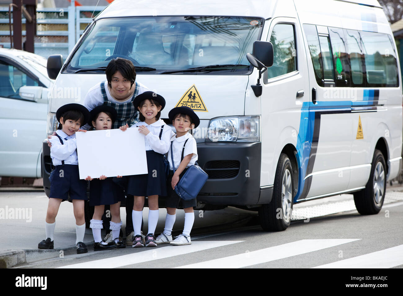 Insegnante di scuola materna e bambini in piedi nella parte anteriore del bus di scuola Foto Stock