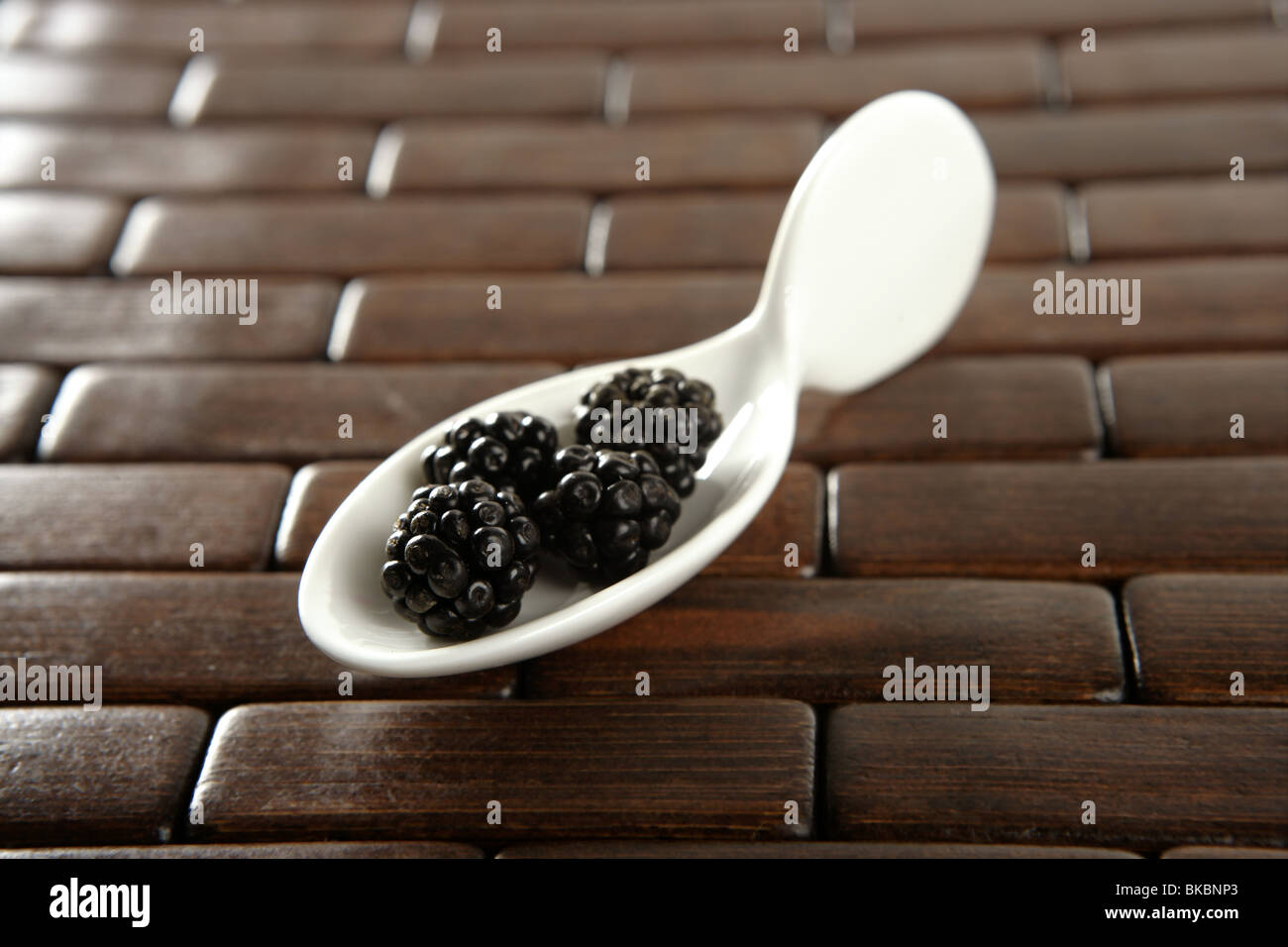 Bacche di colore nero in un cucchiaino di colore bianco e lo sfondo in legno Foto Stock