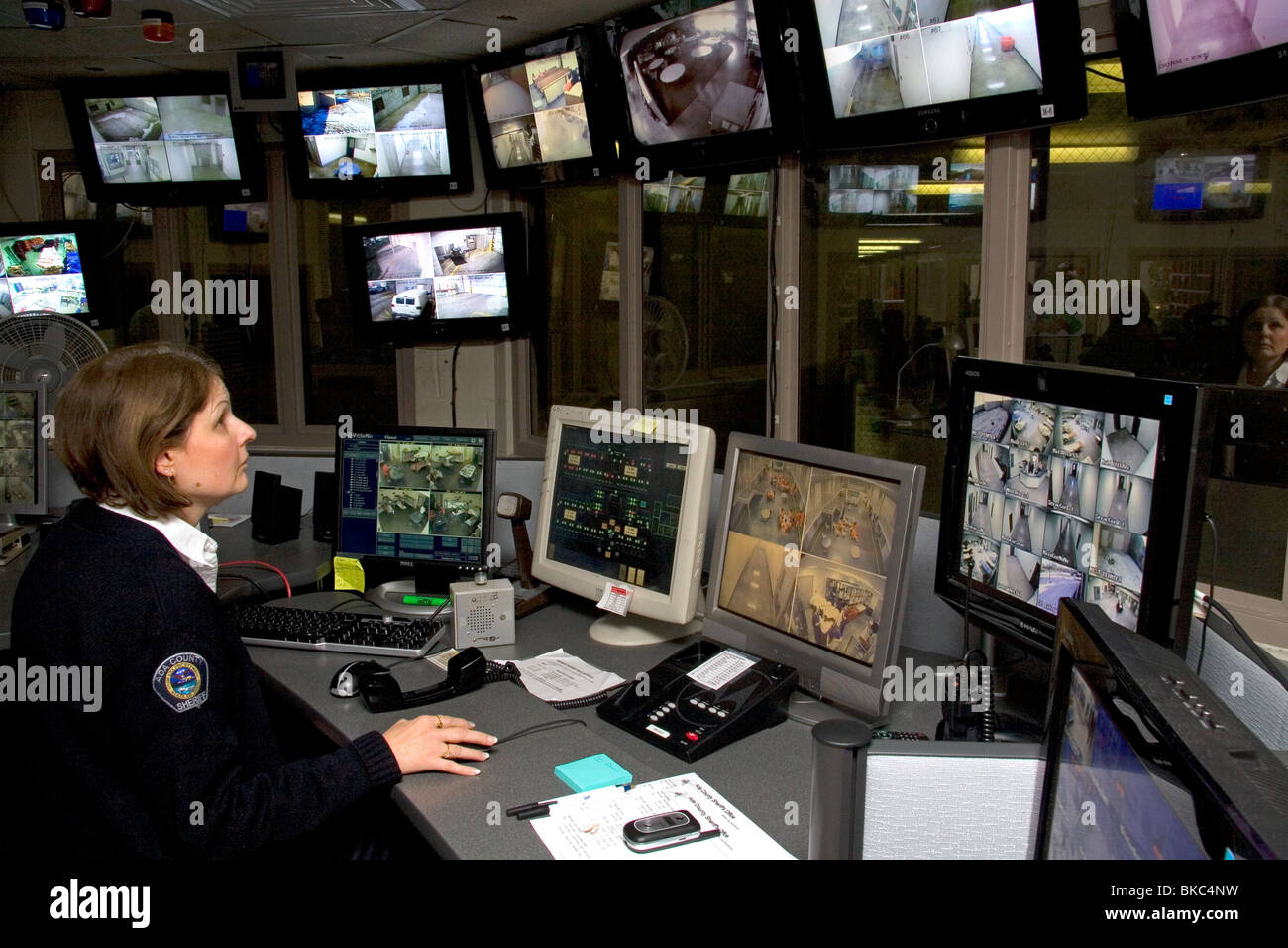 Carcere sala di controllo per la sicurezza con la femmina officer utilizzando video monitora e controlla in remoto le porte. Foto Stock