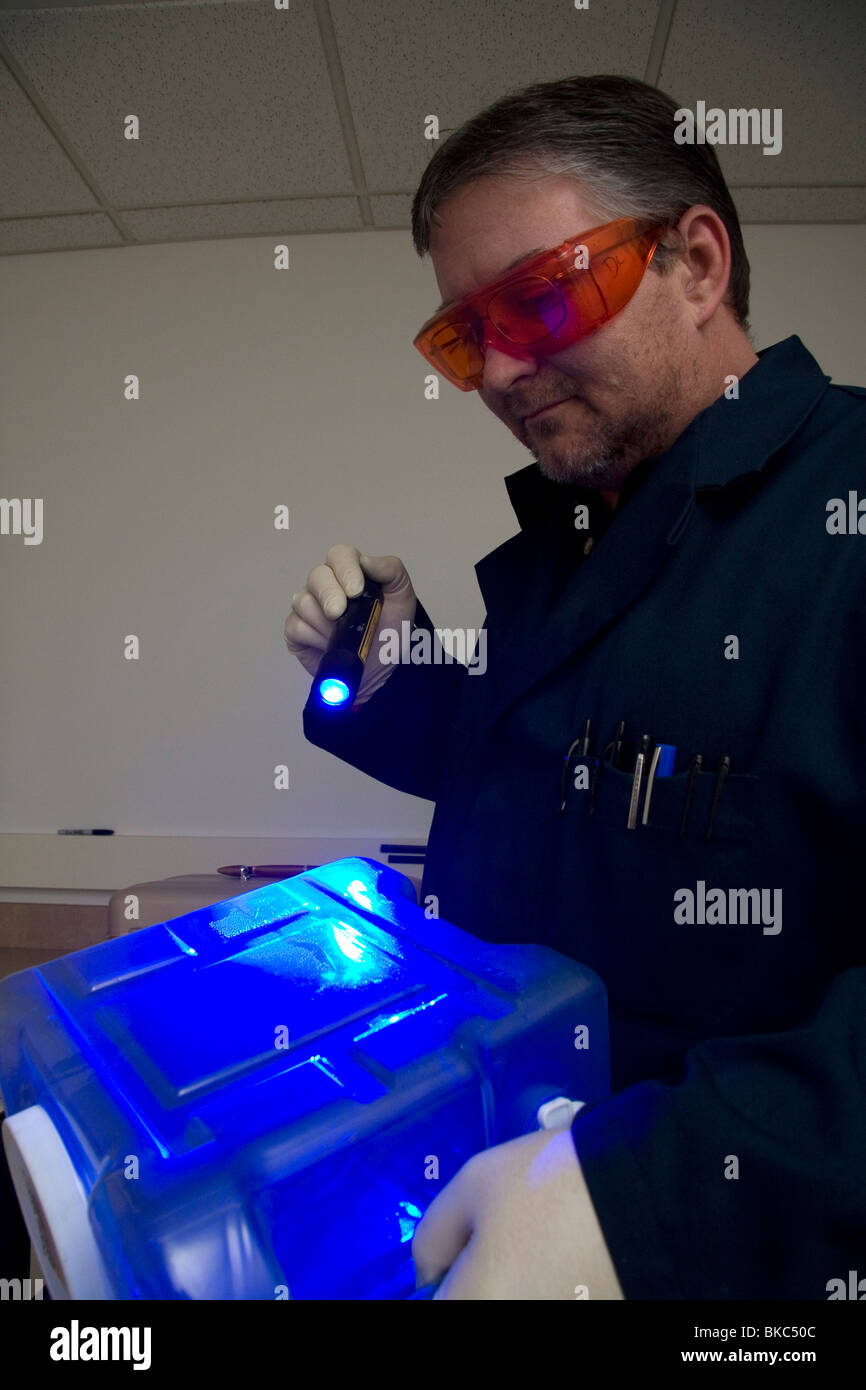 Analista di impronte digitali utilizzando una sorgente di luce colorata per illuminare le impronte digitali su prove forensi in un laboratorio del crimine. Foto Stock