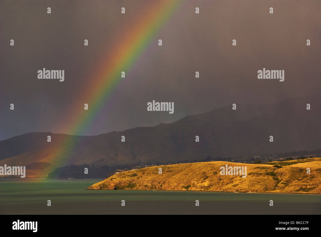 Un arcobaleno nel passaggio di docce a pioggia sul mare con colline costiere in background. Foto Stock