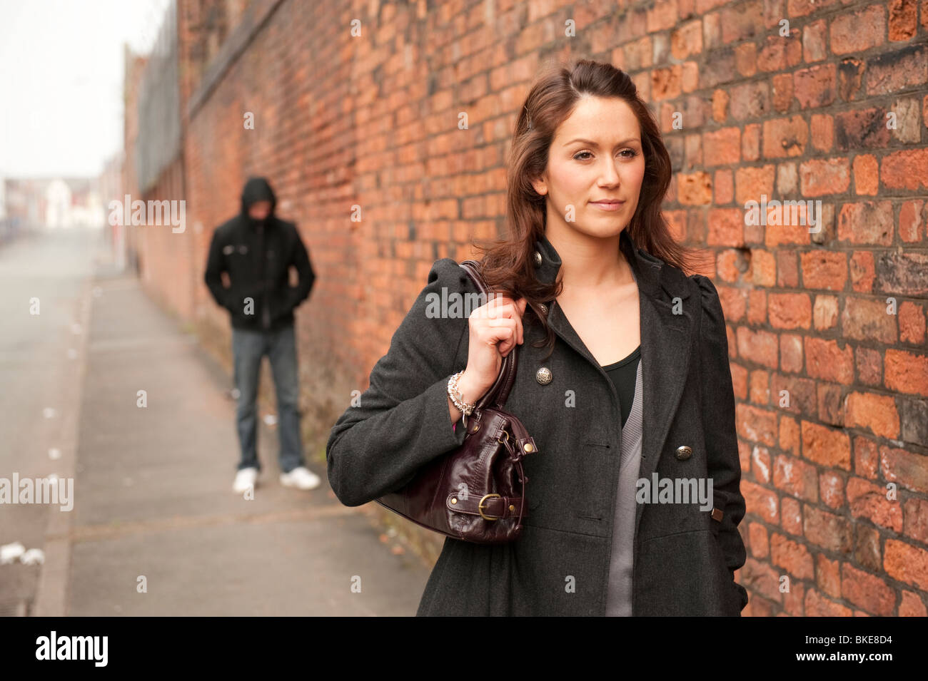 Lone donna camminando lungo la strada con borsetta e thug / penale in background poste dai modelli. Modello completamente rilasciato Foto Stock