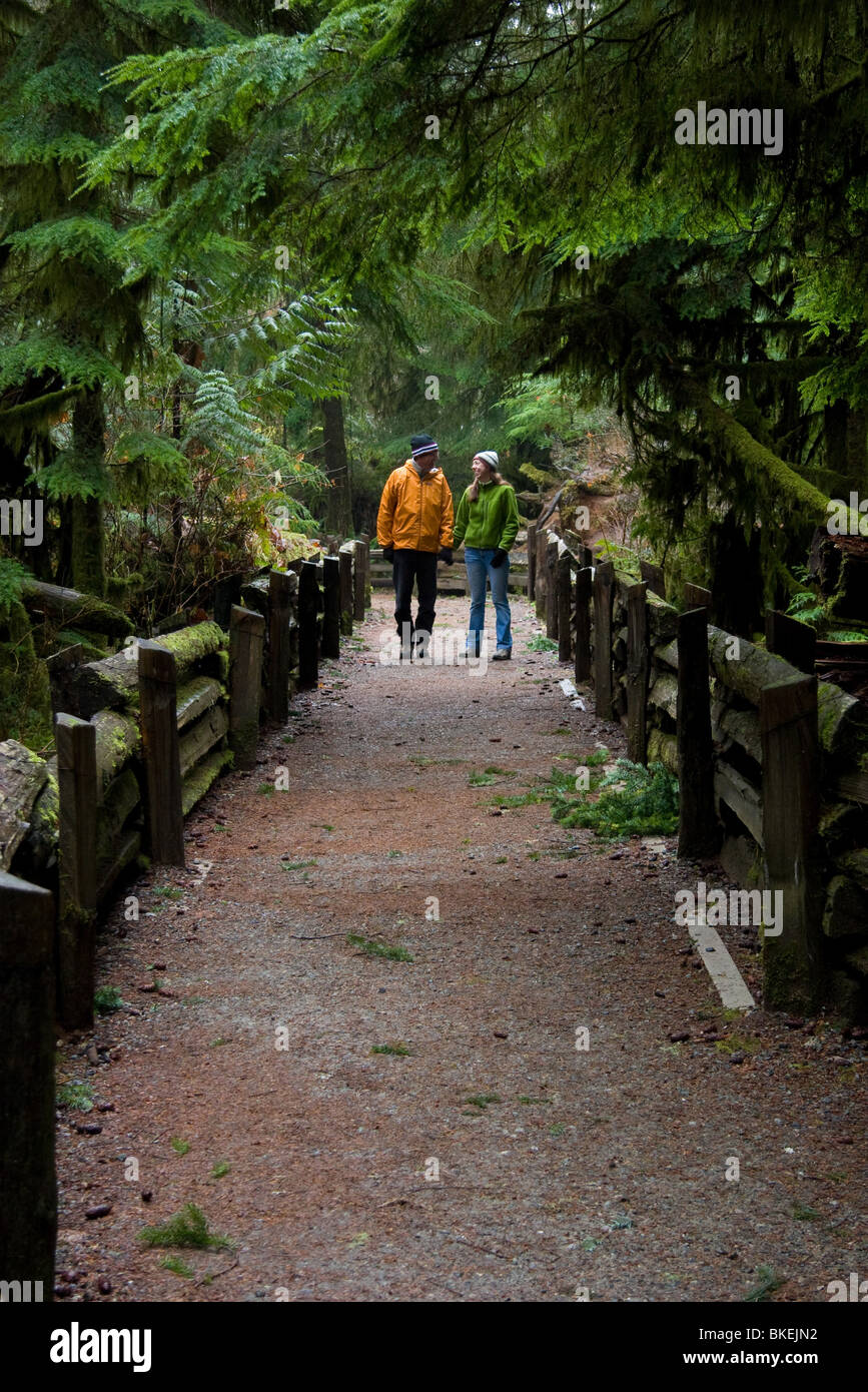 L uomo e la donna a piedi giù per un sentiero in una vecchia foresta, Cattedrale Grove, BC, Canada Foto Stock