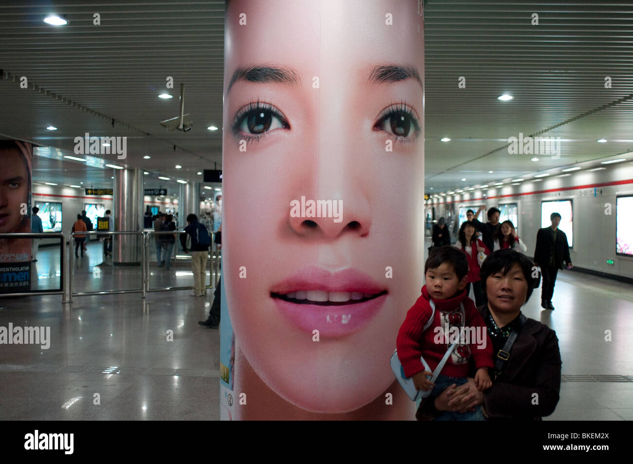 Una donna che porta un bambino passeggiate nei pressi di una grande pubblicità di moda in una stazione della metropolitana, Shanghai, Cina Foto Stock