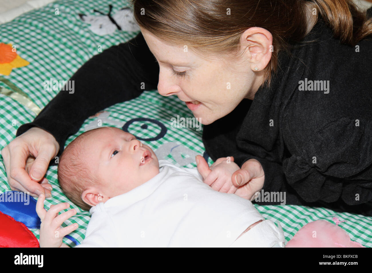 La madre e il neonato ragazzo su un tappeto gioco cercando in ogni altri occhi la madre è consolante il bambino tenendo le mani Foto Stock
