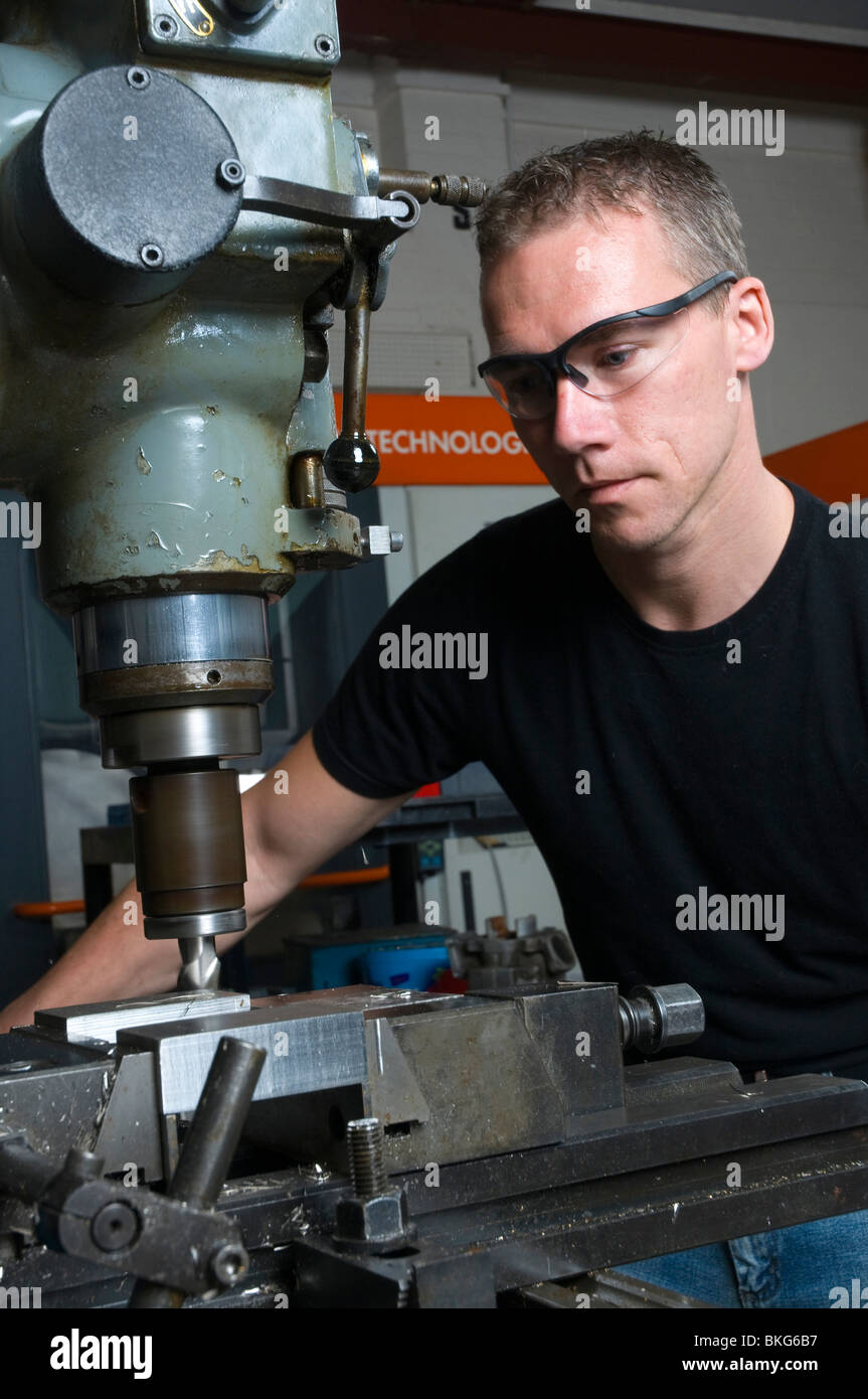 Un ingegnere di precisione nella sua bottega utilizzando una macchina di fresatura che indossa gli occhiali di protezione. Foto Stock