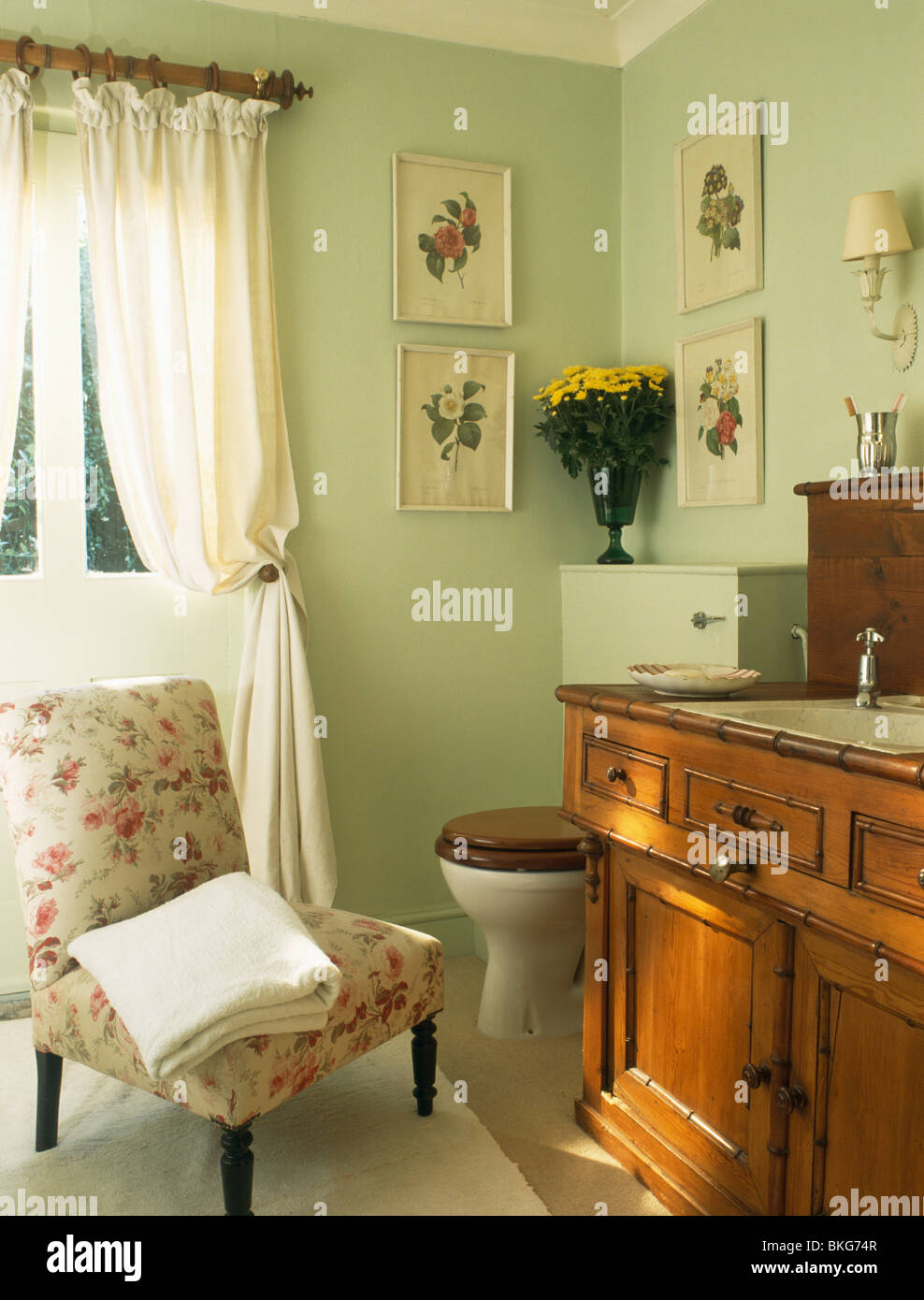 Floral sedia imbottita e tende color crema in verde pastello bagno con lavabo inserito nella vecchia credenza in legno Foto Stock