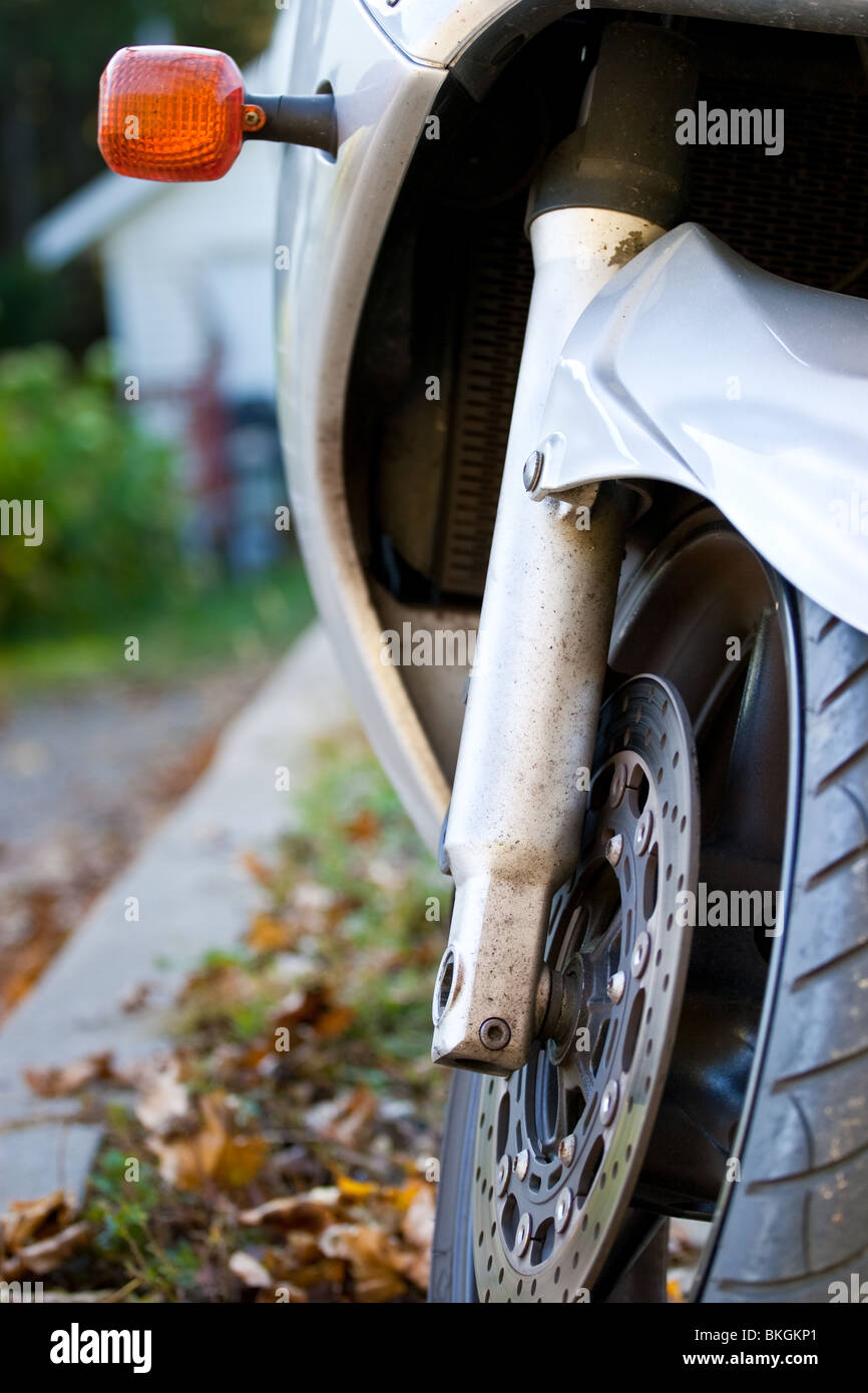 Un primo piano di una motocicletta pneumatico, rotore freno e shock, con un arancione segnale di sterzata visibile. Girato a livello degli pneumatici. Foto Stock