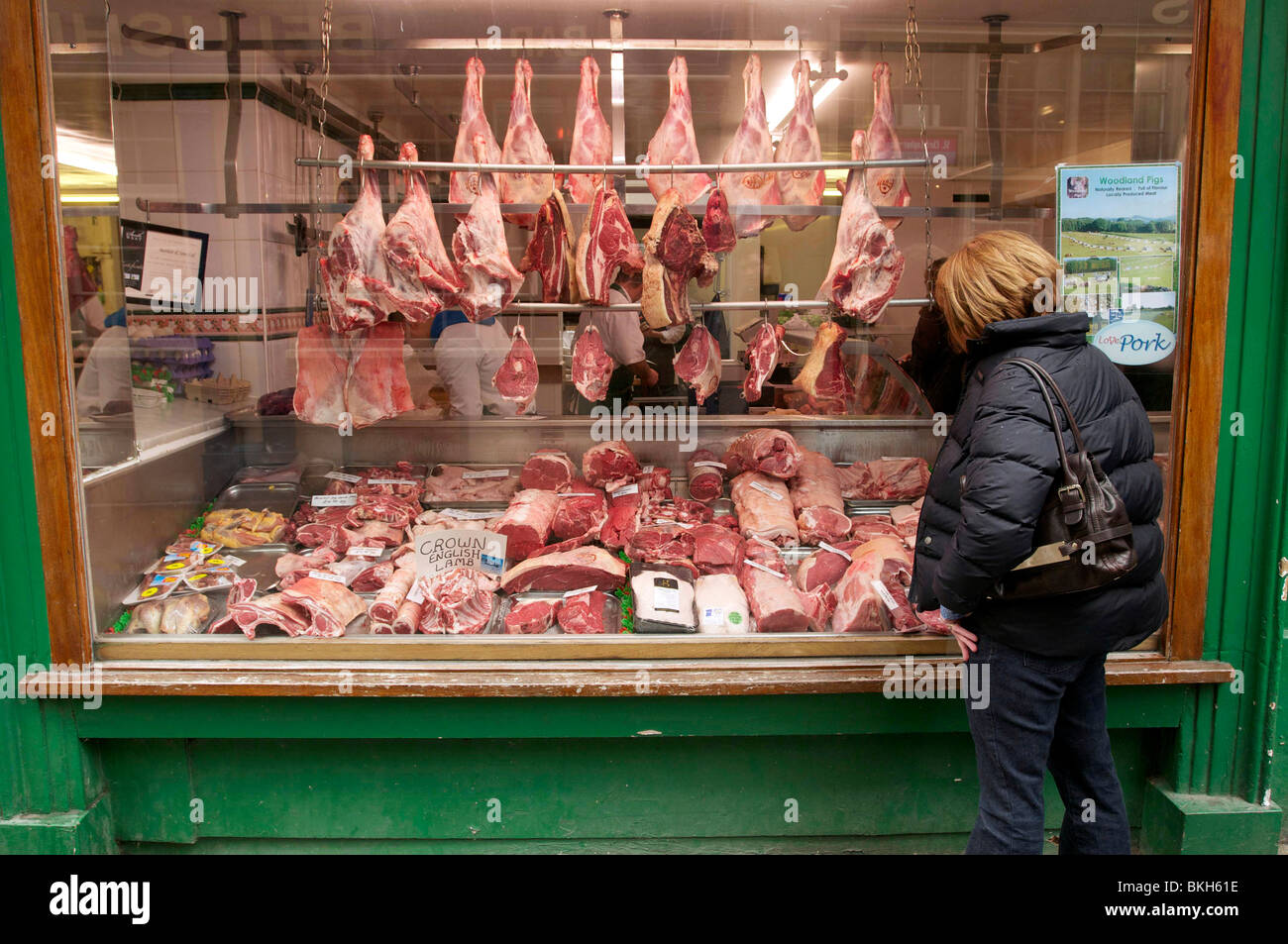 La carne si blocca sul display in un tradizionale negozio di macellaio finestra con una donna che guarda. Foto Stock