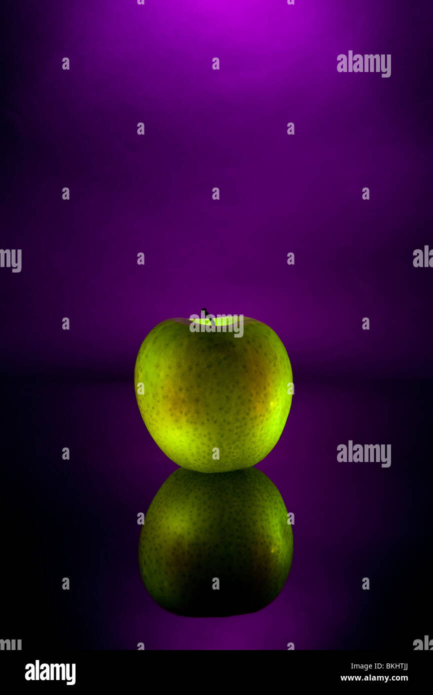Una mela verde su una superficie riflettente con uno sfondo viola Foto Stock