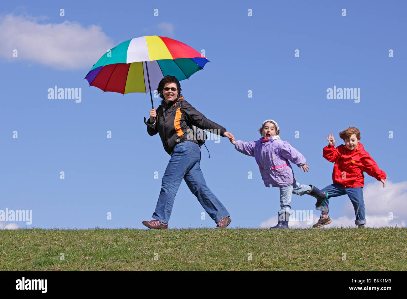 Una madre e i suoi due figli piccoli a piedi lungo una diga con un ombrello coloratissimo Foto Stock