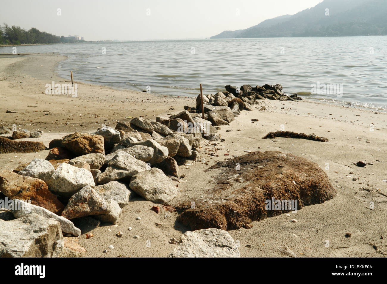 Una immagine di una spiaggia di sabbia dorata con un mare di pietra di barriera. Foto Stock