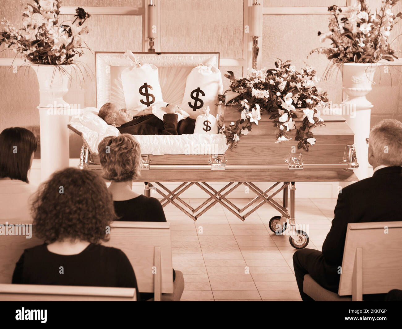 Il defunto giacente in una bara al suo funerale con sacchi di denaro che lo circonda Foto Stock