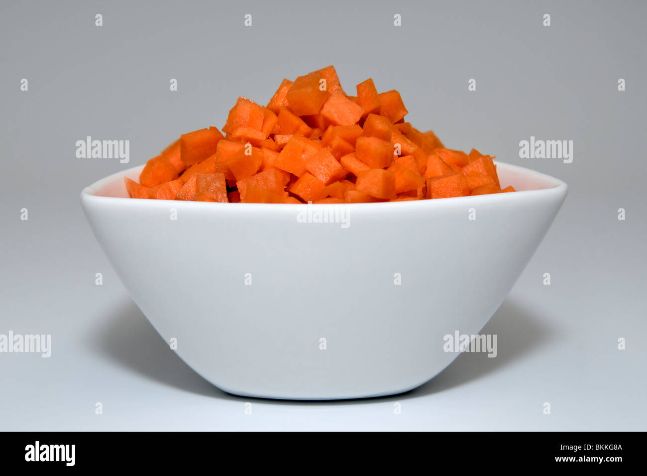 Studio shot di carote tagliate a dadini in bianco ciotola contro uno sfondo bianco Foto Stock