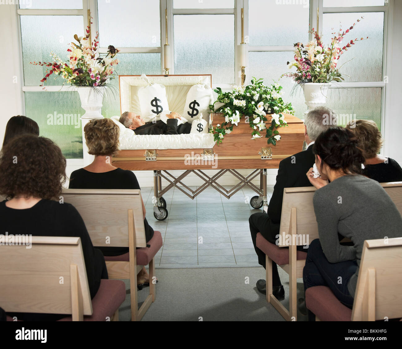 Il defunto giacente in una bara al suo funerale con sacchi di denaro che lo circonda Foto Stock
