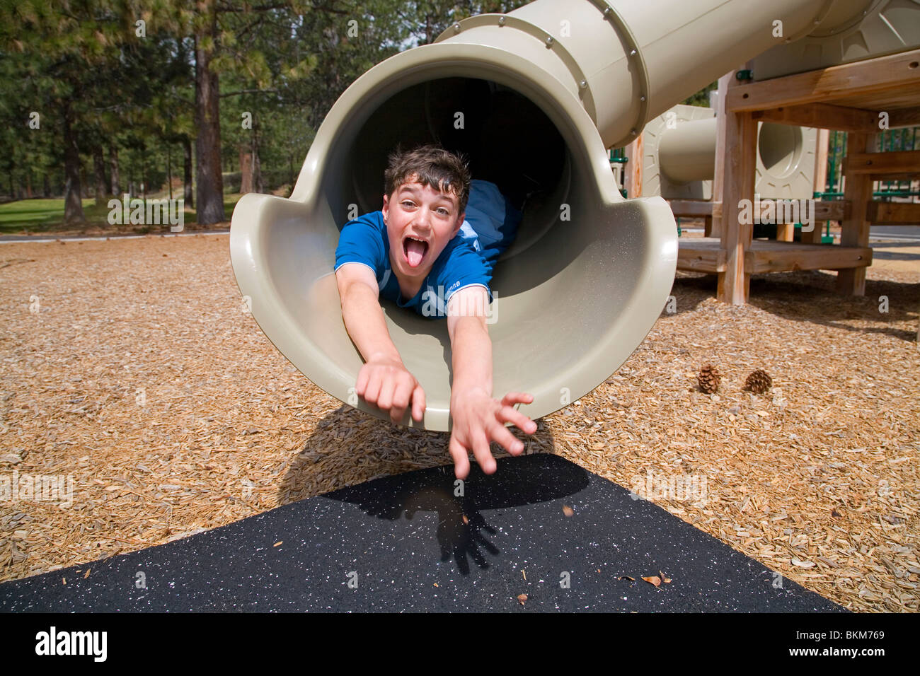 Middle School boy su un parco giochi slitta, facendo una faccia Foto Stock