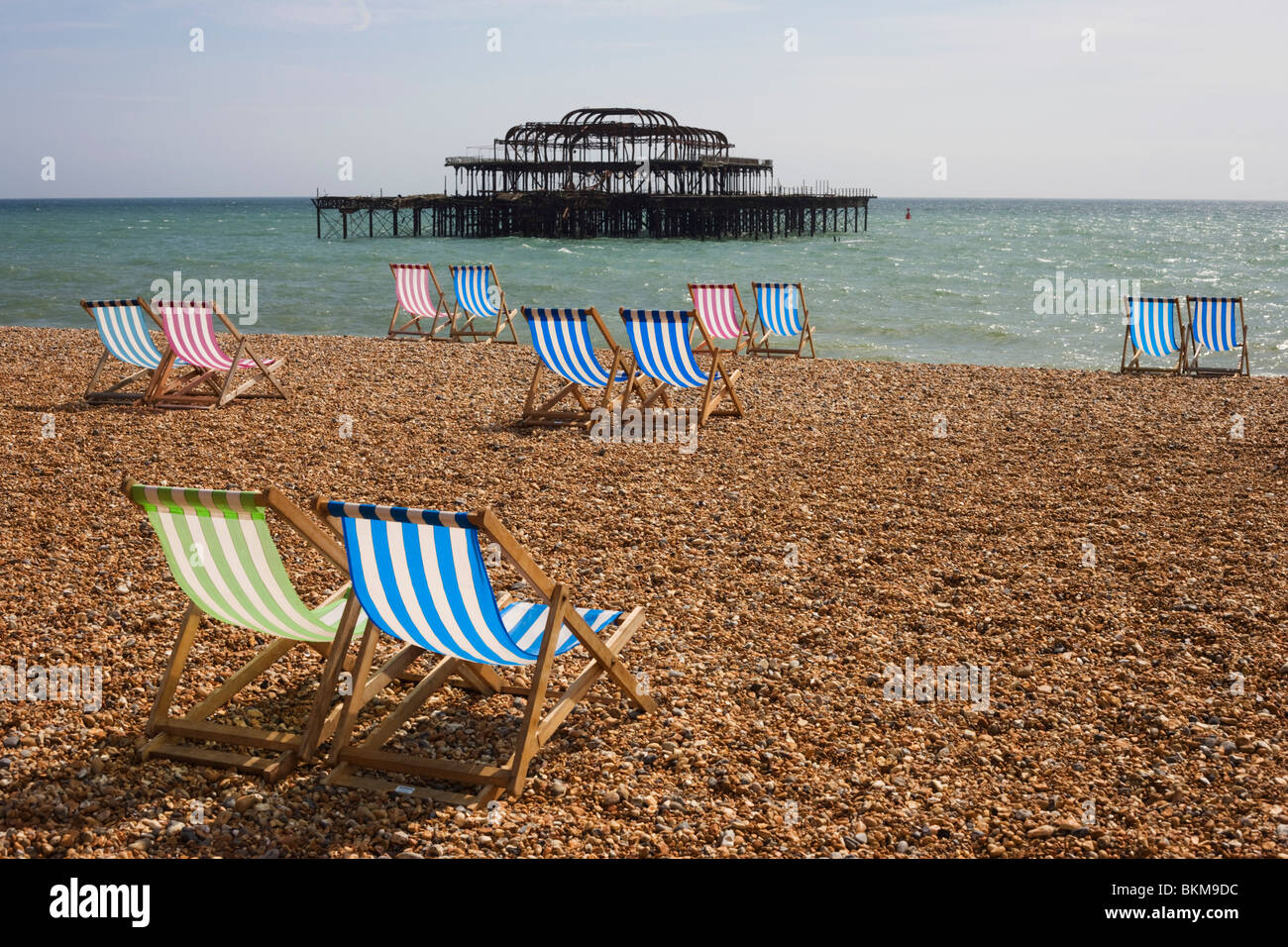 Brighton spiaggia ghiaiosa di sedie a sdraio e rovinato Molo Ovest. Foto Stock