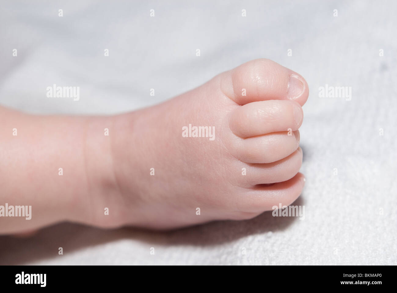 Vicino sul piccolo piede della bambina con punte arricciate contro la coltre bianca Foto Stock