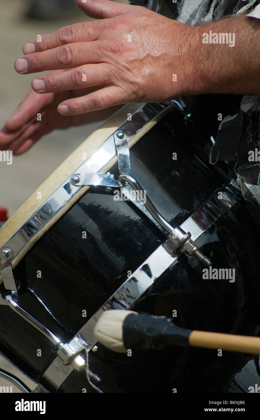 Close up di un percussionista con le mani in mano la riproduzione di un tamburo per accompagnare le danze a Upton Folk Festival, con coscia in primo piano Foto Stock