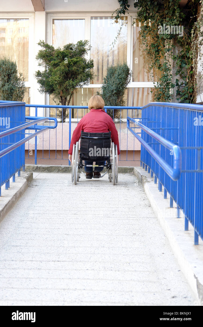 Donna disabile su sedia a rotelle entrata del palazzo utilizzando la rampa per disabili Foto Stock