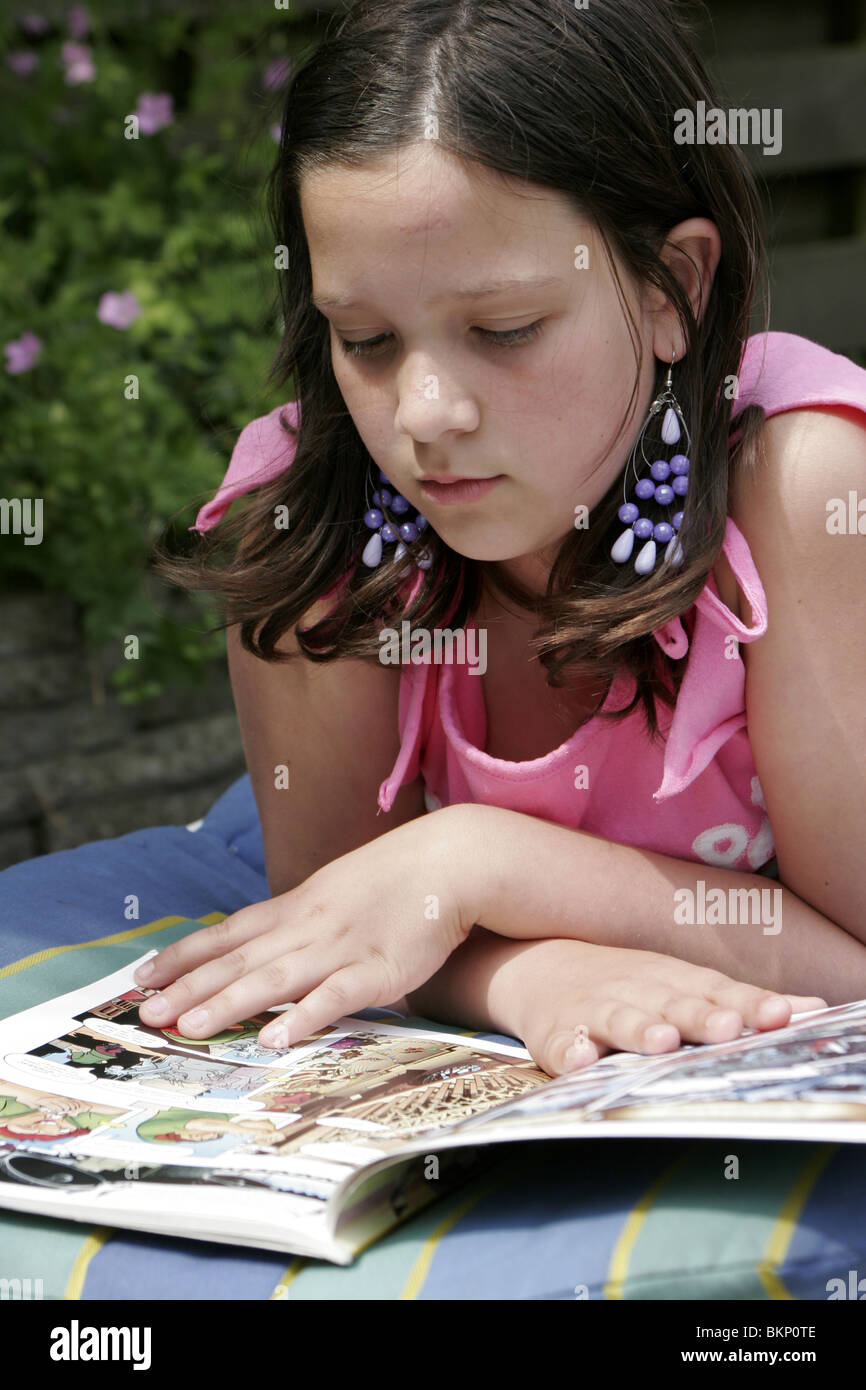 Ragazza adolescente rilassante al di fuori e la lettura di un libro a fumetti. Foto Stock