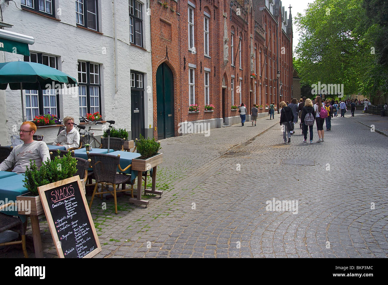 Le persone a rilassarsi in un cafe' all'aperto a fianco di una strada a Bruges, Belgio Foto Stock