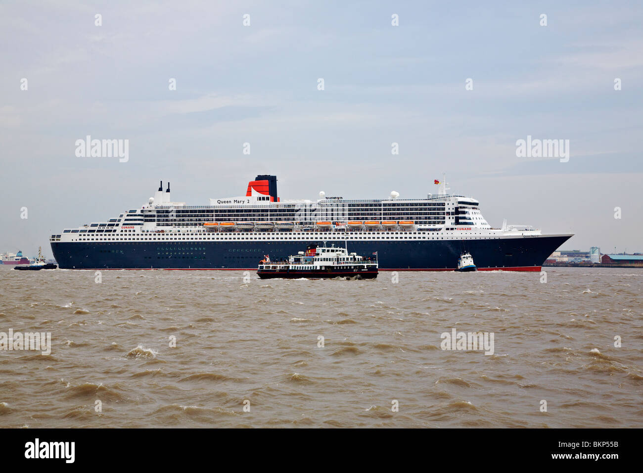 Crociera QUEEN MARY 2 in visita a Liverpool con i rimorchiatori che assiste e Mersey ferry crossing di fronte a lei Foto Stock