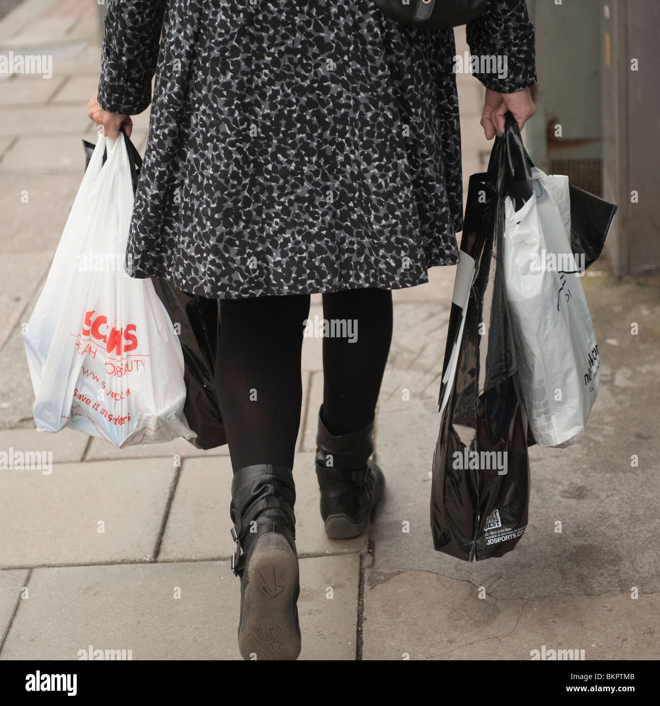 Vista posteriore di una donna shopper che trasportano molti sacchi di plastica di acquisti, REGNO UNITO Foto Stock