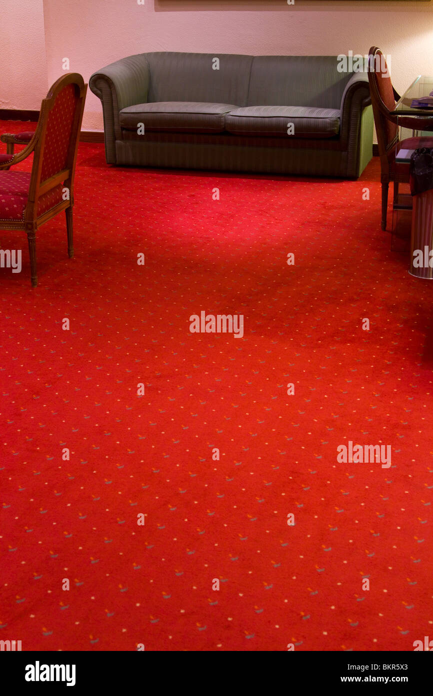 Sparse mobili e un luminoso tappeto rosso in un budget hotel lobby. Foto Stock