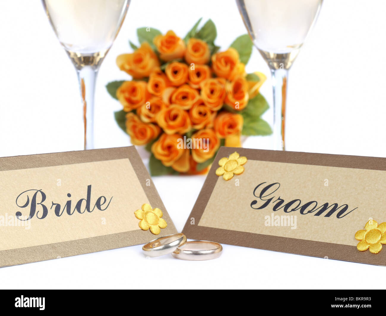 Sposa e lo Sposo schede con nome, gli anelli di nozze, due calici da bianco e sposa giallo del bouquet di rose in background Foto Stock