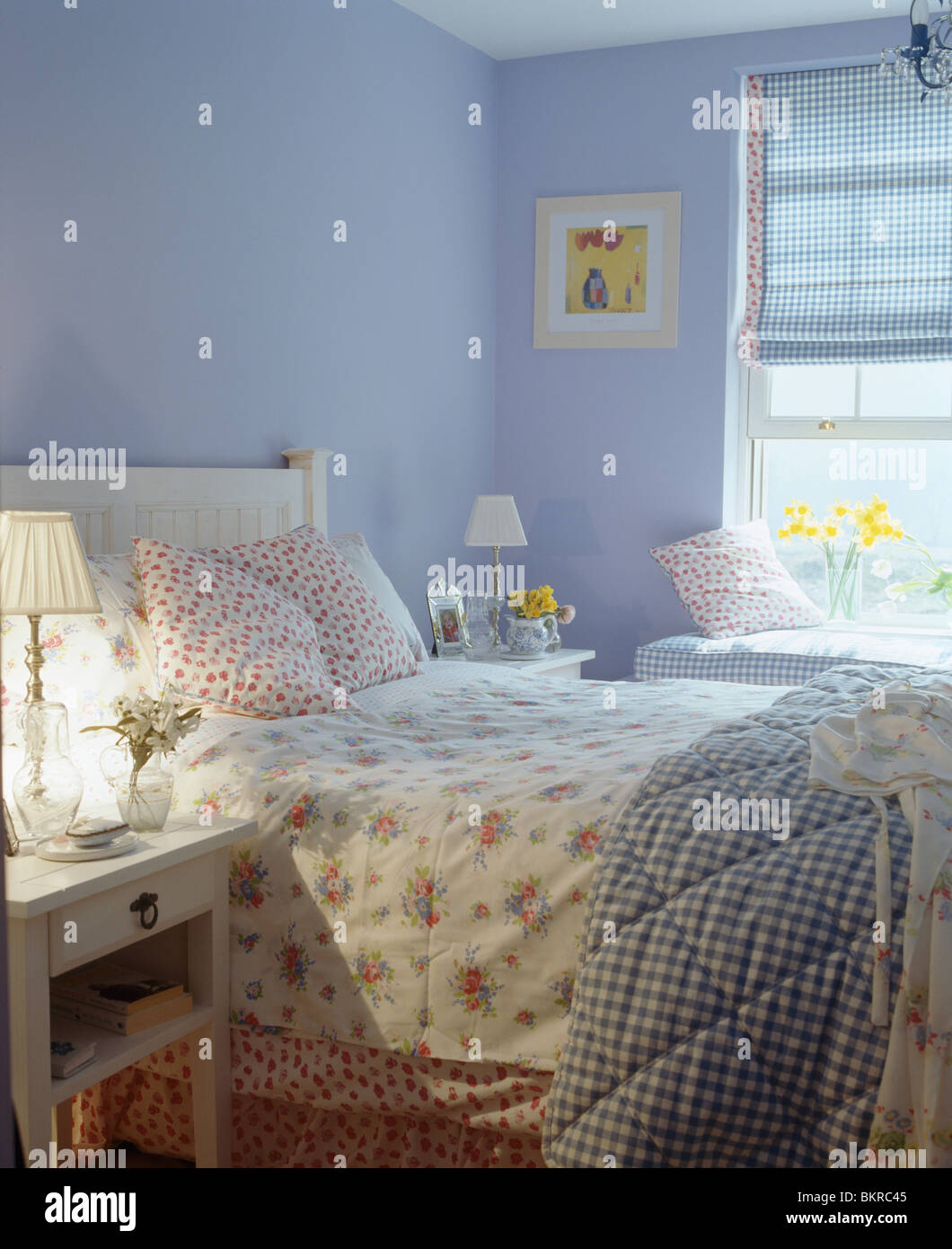Floral biancheria da letto e verificato su quilt letto nel paese di malva camera da letto con blue cieco sulla finestra e acceso la lampada sul comodino Foto Stock