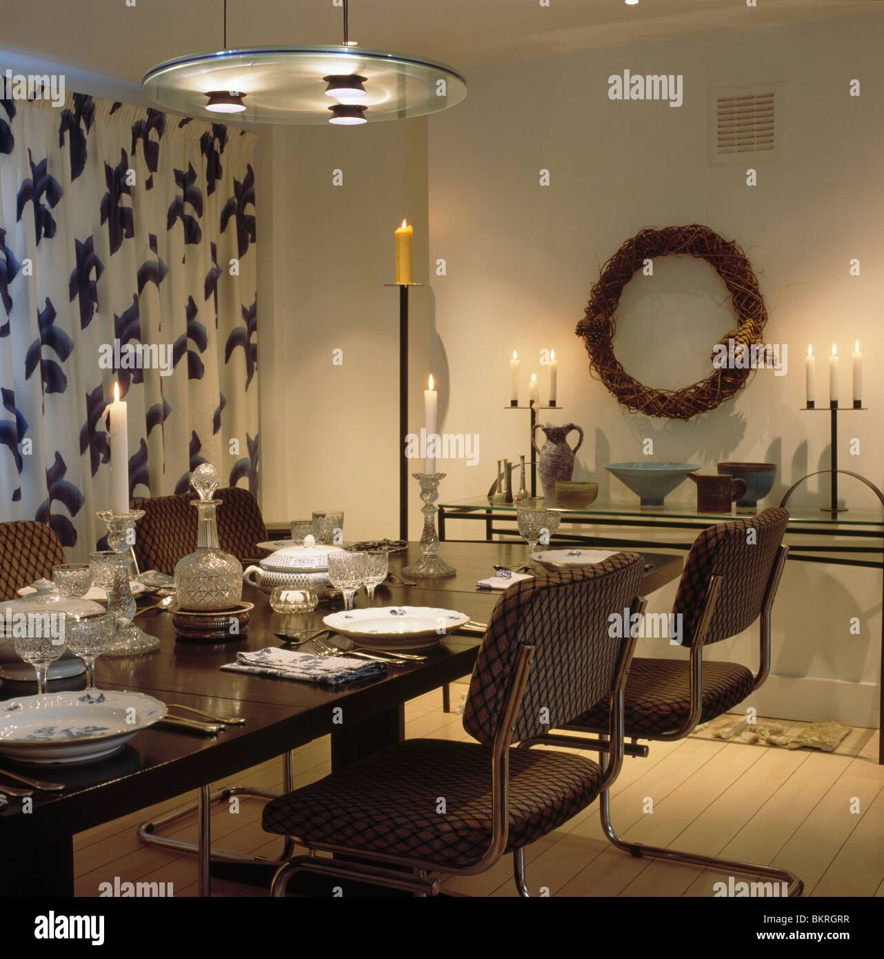 Luce circolare sopra il raccordo tavola nera in sala da pranzo con nero+bianco tende a motivi geometrici candele accese sul tavolo console Foto Stock