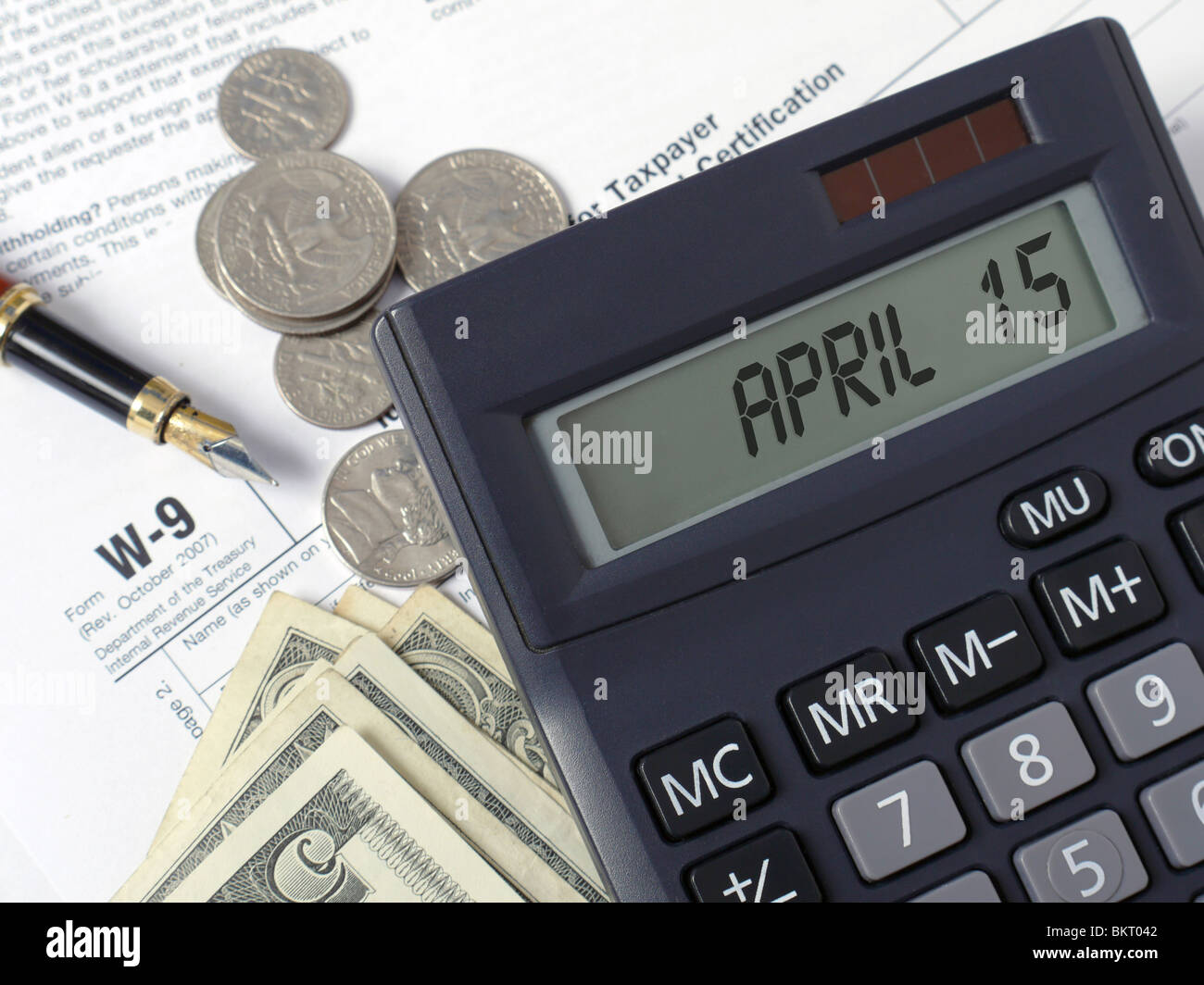 Calcolatrice con display LCD per la visualizzazione aprile 15 collocato su W-9 le imposte sul reddito dei moduli con penna e dollari americani Foto Stock