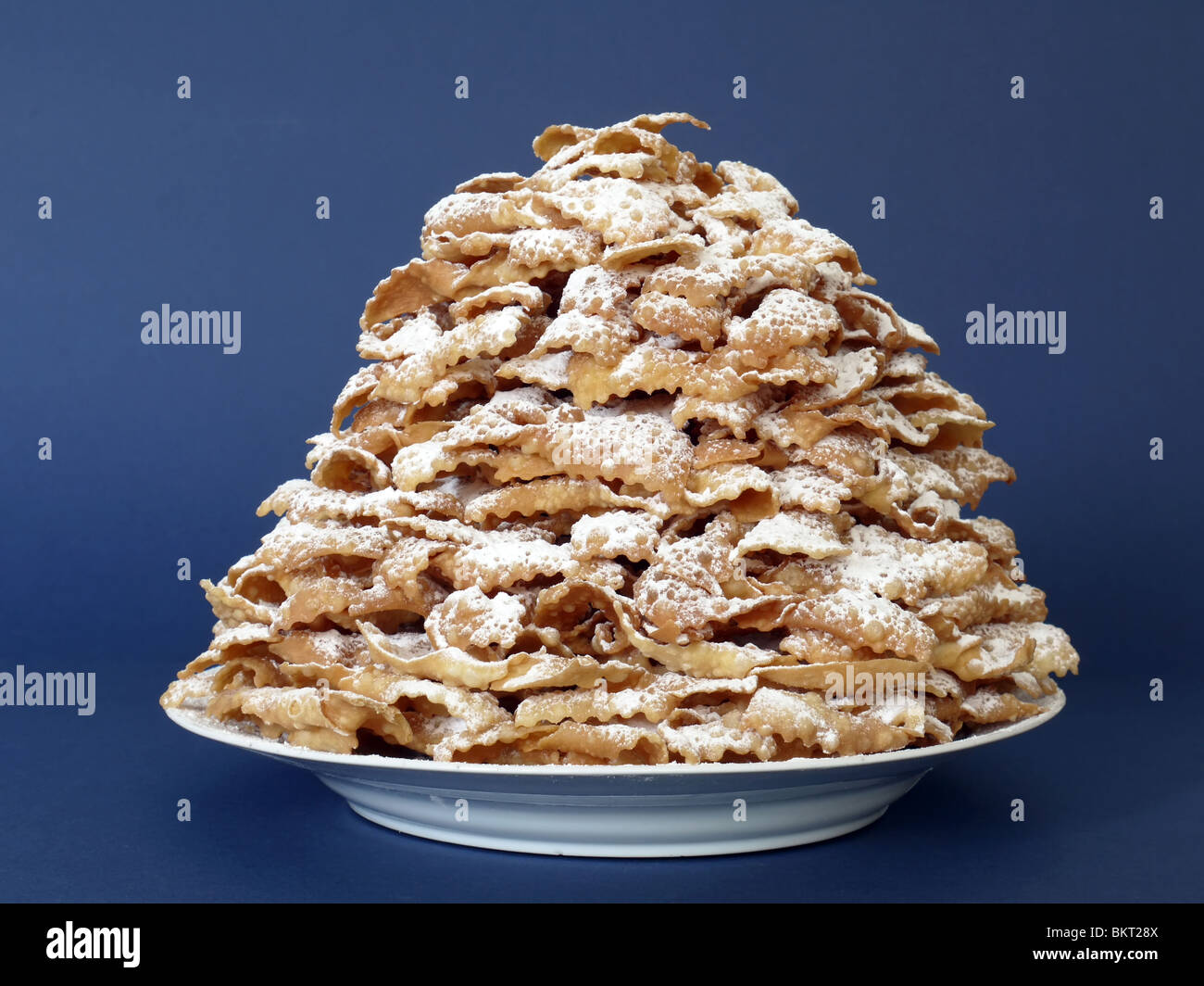 Piatto pieno del tradizionale dolce polacco biscotti croccanti chiamato Faworki con lo zucchero semolato su sfondo blu scuro Foto Stock