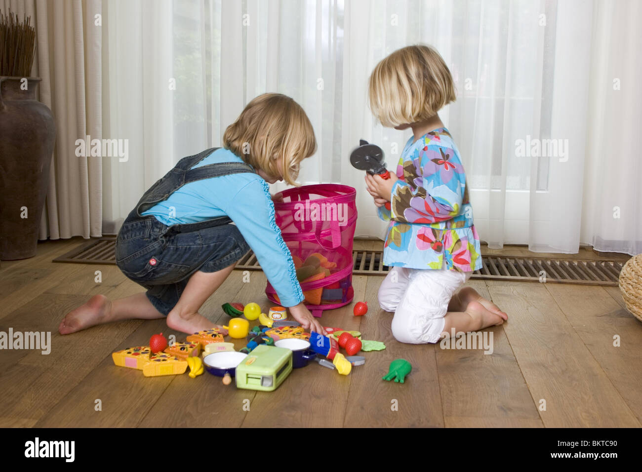 Due giovani bambini chiaro dai giochi all'interno, le bambine sono mettendo i giocattoli nel bambino Cestello portaoggetti a casa, cooperare Foto Stock