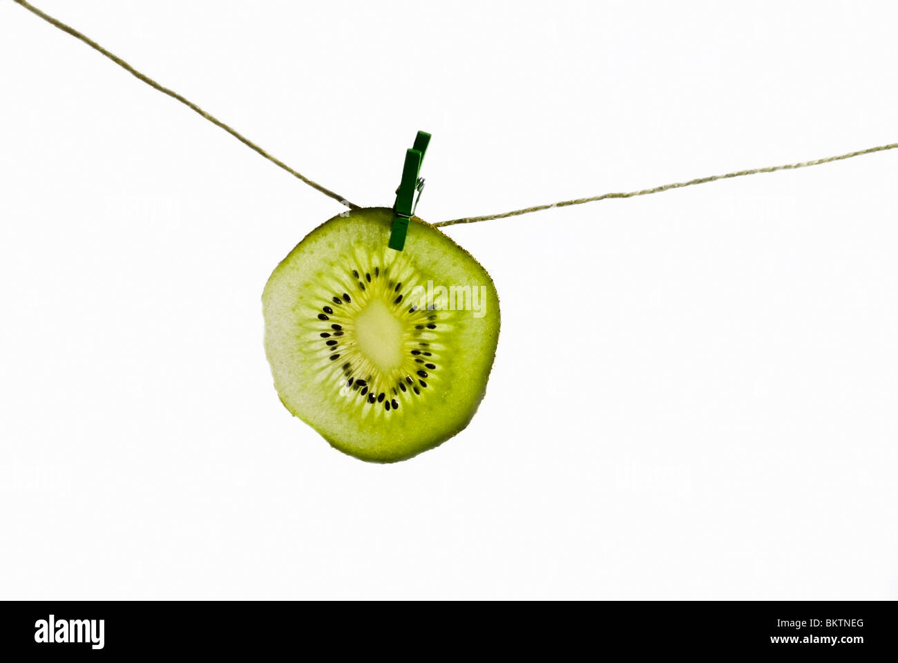 Una fetta di kiwi impiccato da una corda con una molletta da bucato per asciugare Foto Stock