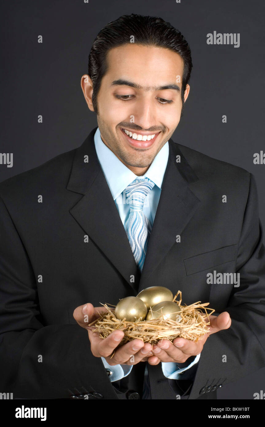 Imprenditore azienda nido con Golden Egg, sorridente Foto Stock
