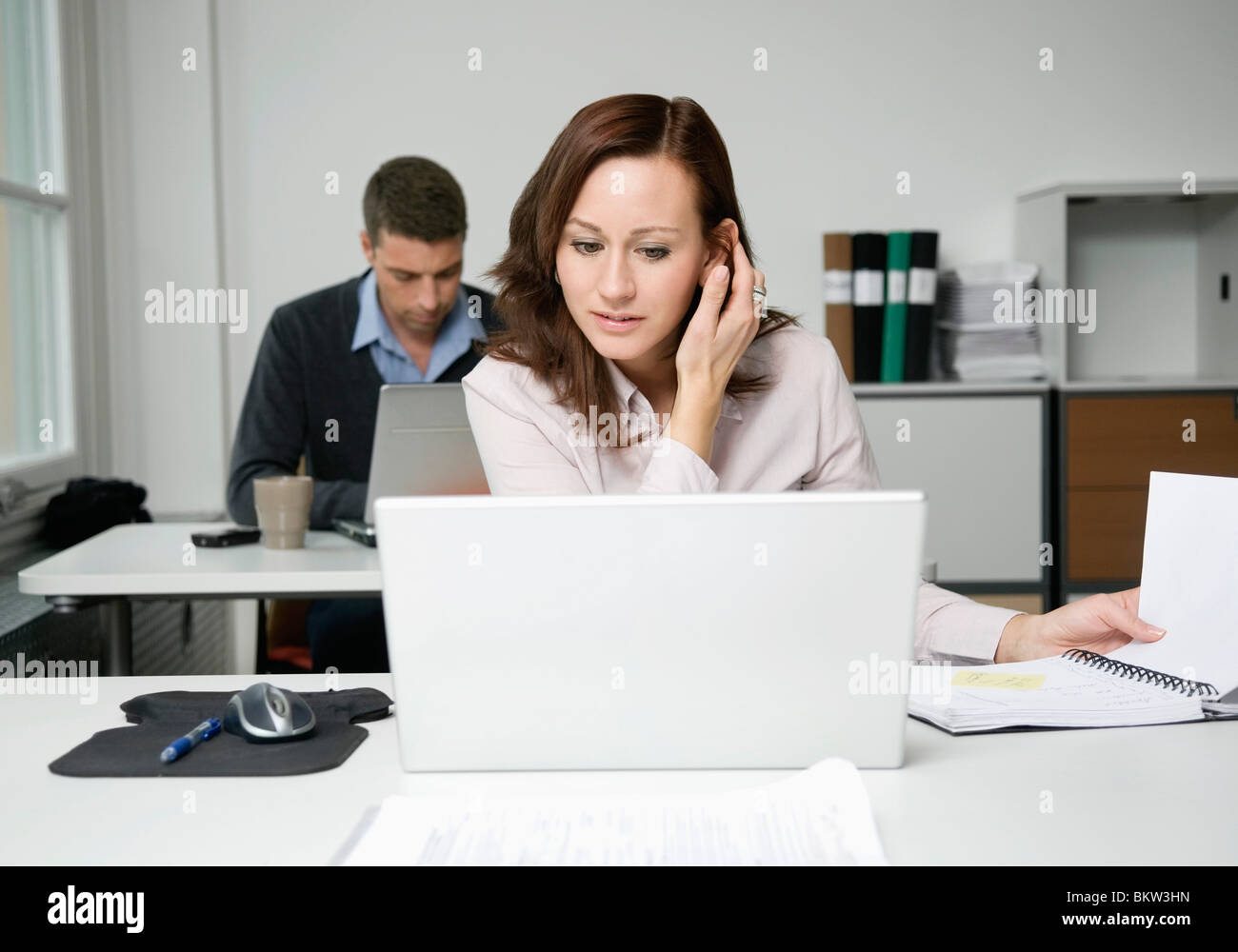 Donna che guarda al portatile, collega di lavoro in background Foto Stock