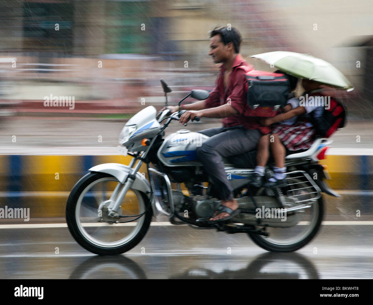 India, Uttar Pradesh, Agra, motociclista e passeggeri bambini in forti piogge monsoniche Foto Stock