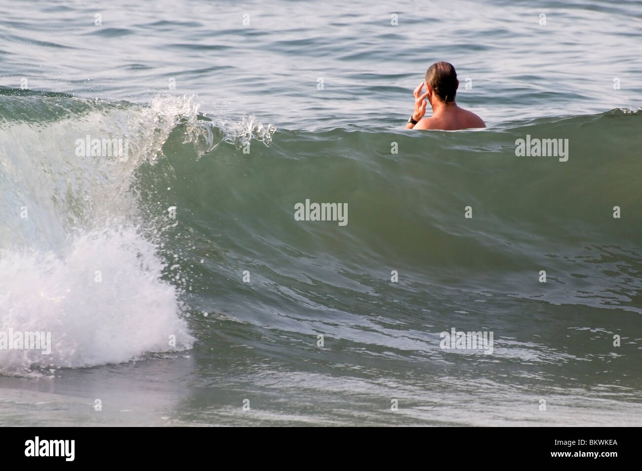 Adulto maschio senior tenta di rimuovere l'acqua dal suo orecchio dopo il nuoto attraverso una grande onda. Foto Stock