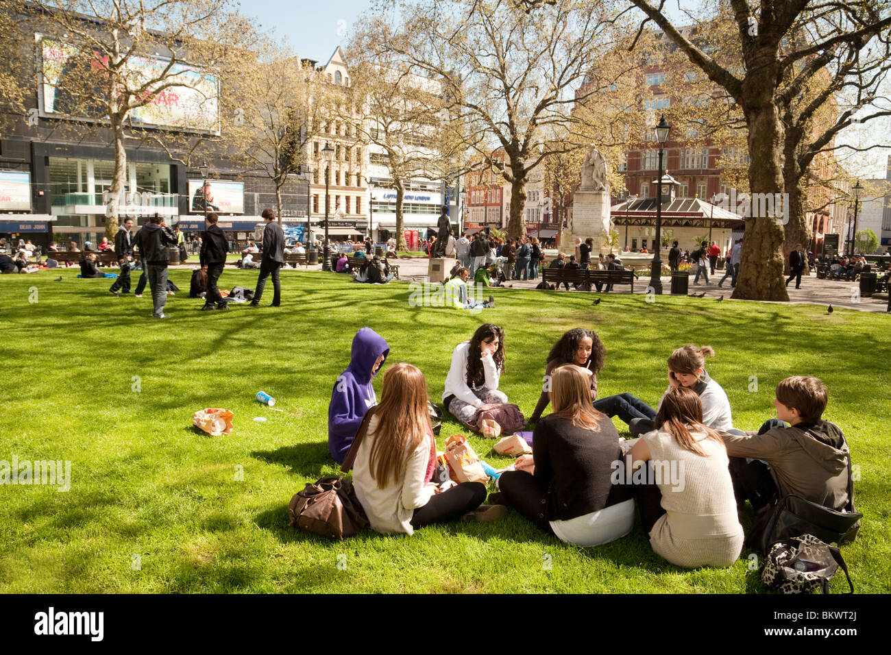 Un gruppo di adolescenti seduti sul prato in estate il sole, Leicester Square, London REGNO UNITO Foto Stock