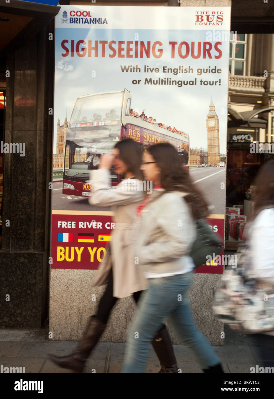 Due ragazze oltrepassando un segno pubblicità London bus tours, Piccadilly Circus, London REGNO UNITO Foto Stock