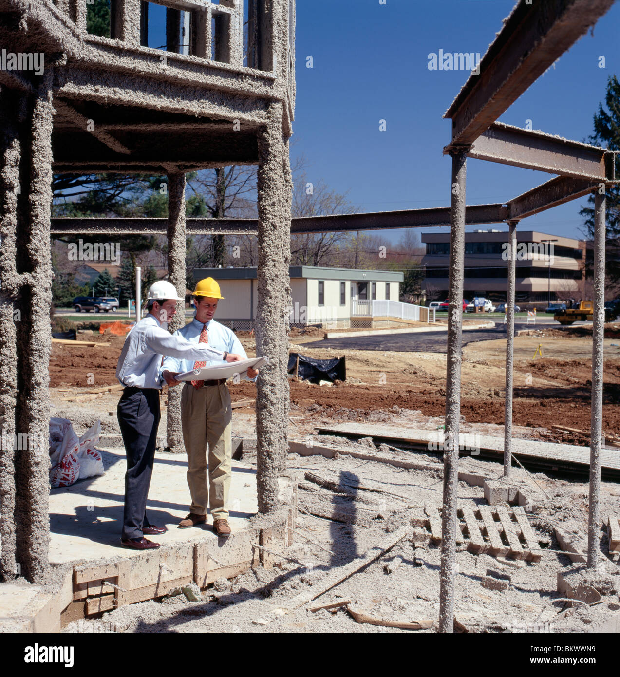 Due dirigenti maschi la revisione di disegni architettonici su un sito di costruzione di un nuovo corporate edificio per uffici Foto Stock