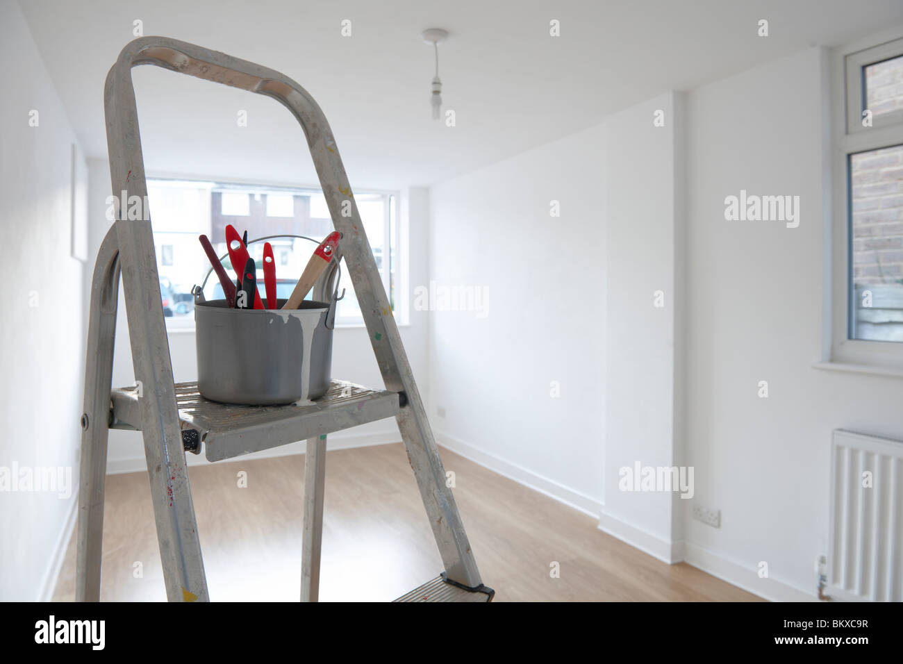 Scaletta con il vaso di vernice e spazzole in piedi nella stanza vuota Foto Stock
