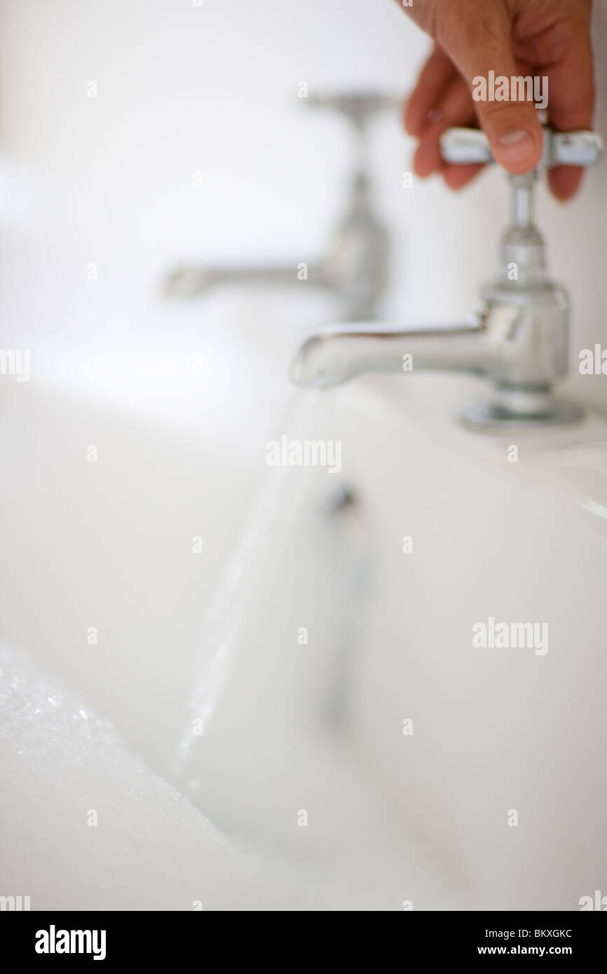 Close up man mano apertura rubinetto bagno con acqua corrente Foto Stock