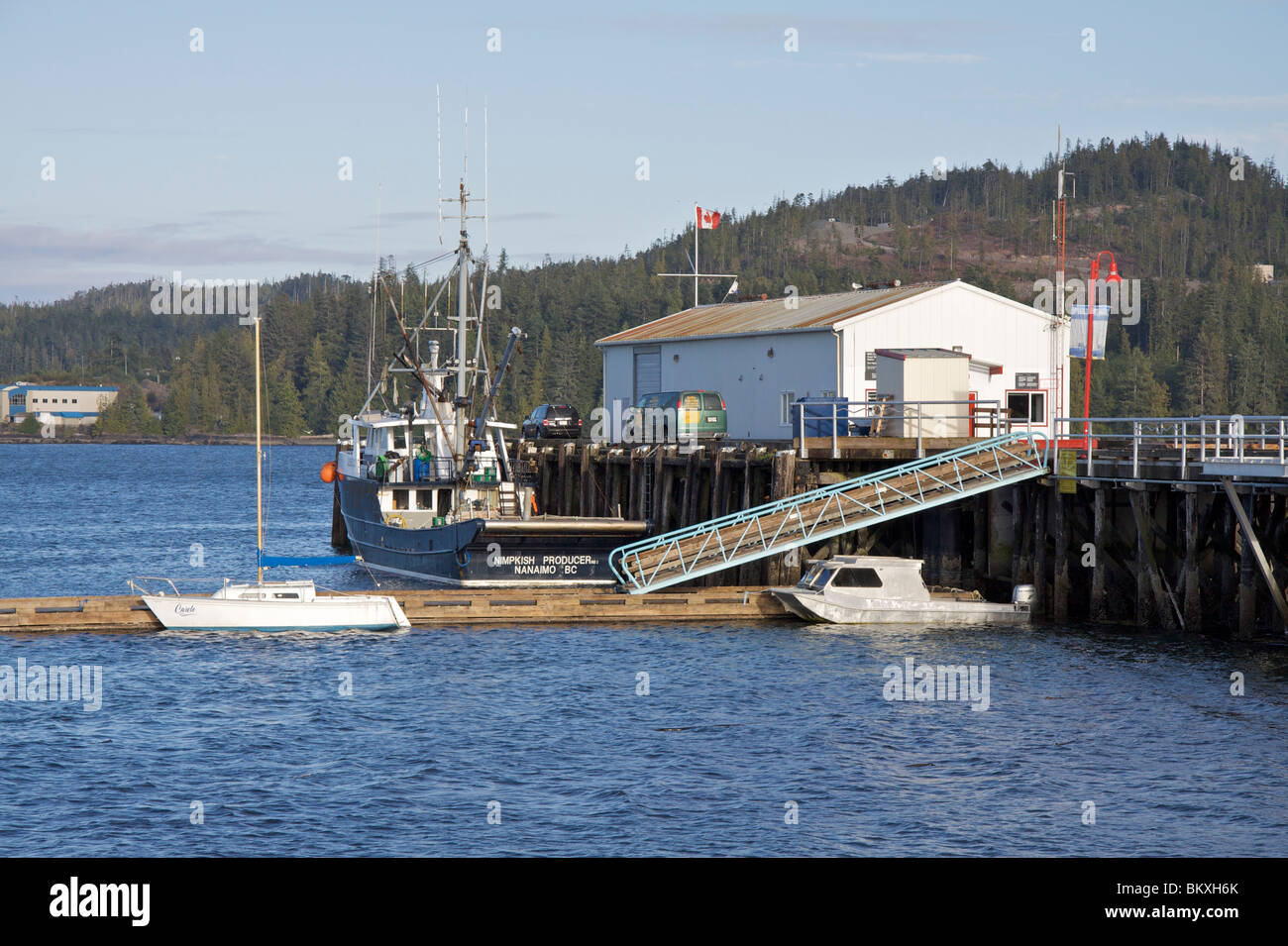 Trawler boat Nimpkish produttore " ormeggiata al Porto Hardy Docks con veicoli e alberi di pino nella distanza attraverso Hardy Bay Foto Stock