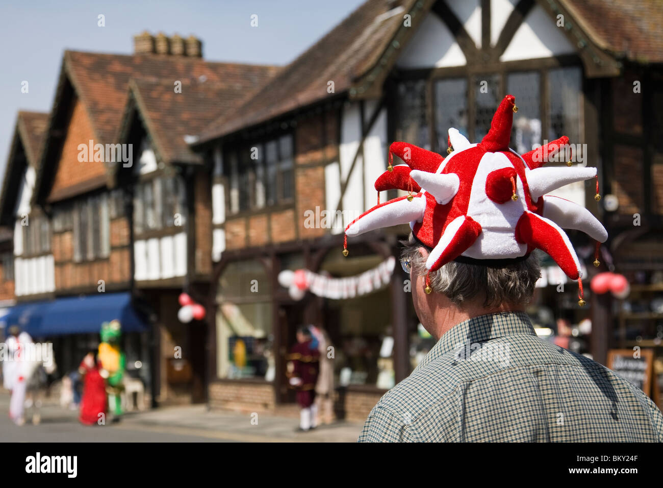 Un curioso indossando un buffone di hat attende una processione su St George's day, Haslemere, Surrey, Inghilterra. Foto Stock