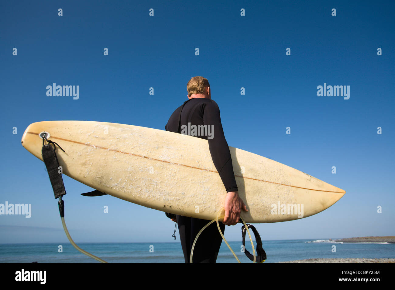 Un uomo sta con la sua tavola da surf sotto il suo braccio sulla costa perso, California. Foto Stock