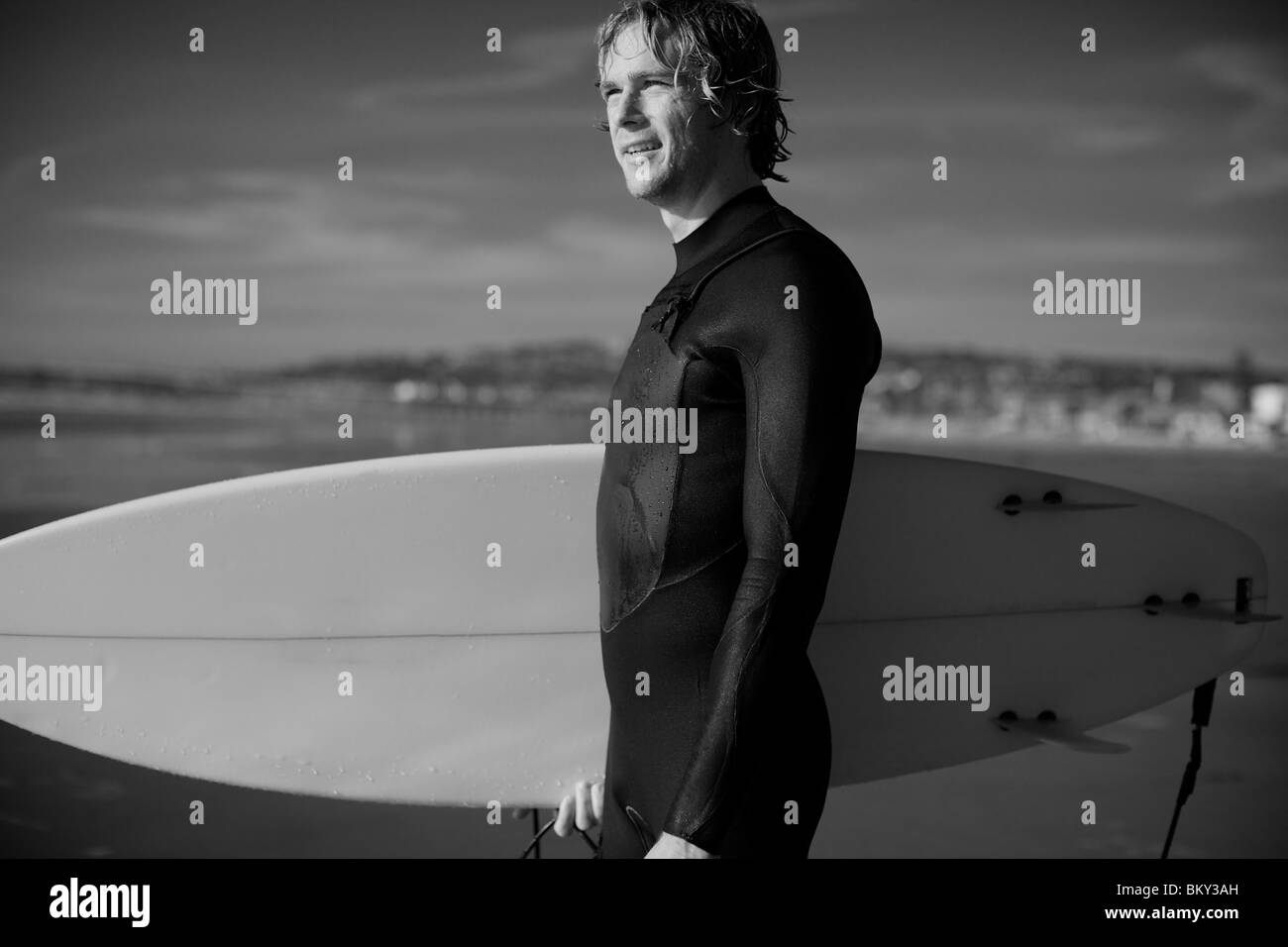 Giovane maschio surfer a Pacific Beach in San Diego California in una giornata di sole guardando lontano dalla telecamera, osservando l'oceano. Foto Stock